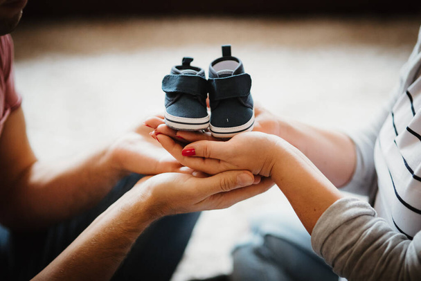 Young future parents holding baby booties shoes in their hands - Fotoğraf, Görsel
