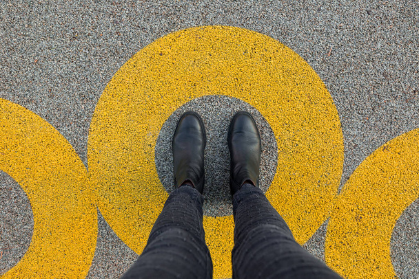 Chaussures noires debout en cercle jaune sur le sol en béton bitumineux. Zone de confort ou concept de cadre. Pieds debout à l'intérieur cercle
 - Photo, image