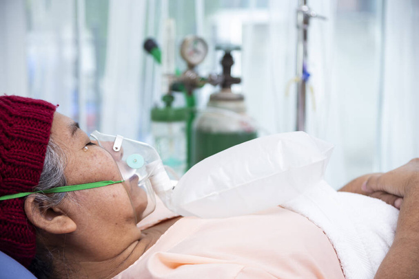 Ázsiai idős nő visel gyapjú kalap oxigén maszkot lélegezni, miközben fekszik a betegágyon, vezető női orvosi és egészségügyi koncepció - Fotó, kép