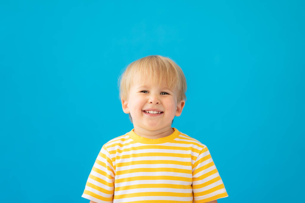 Close up portrait of happy child wearing striped shirt against blue background. Kid having fun on summer vacation - Photo, image