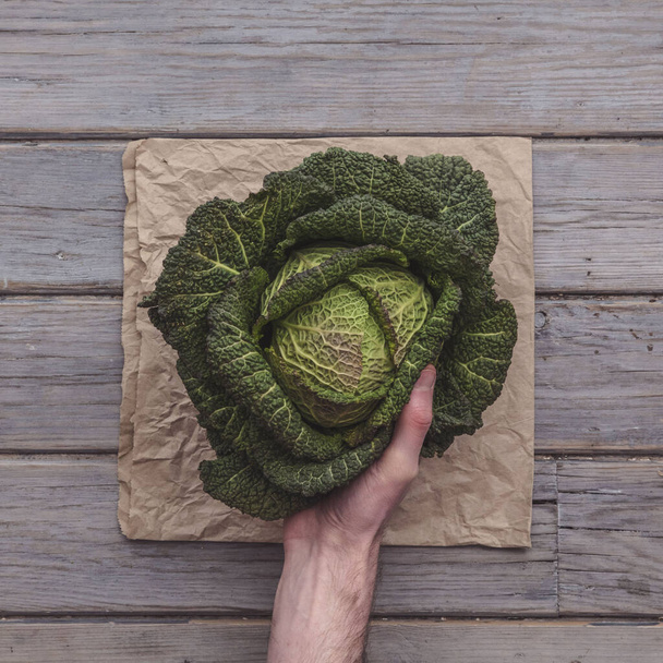 A male hand holding a fresh cabbage against a rustic background - Fotografie, Obrázek