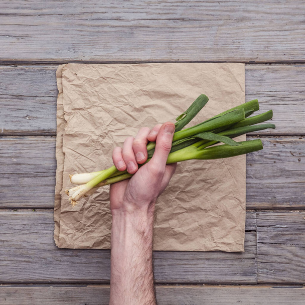 A male hand holding fresh springs onions against a rustic background - Foto, Imagem