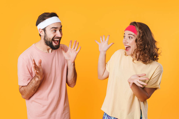 Portrait of athletic young cheerful couple wearing headbands screaming together in surprise isolated over yellow background - Photo, Image