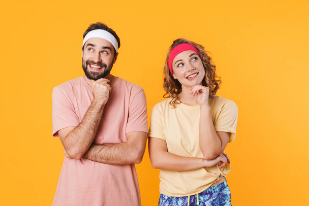 Portrait of athletic young couple wearing headbands thinking and looking upward at copyspace isolated over yellow background - Foto, immagini
