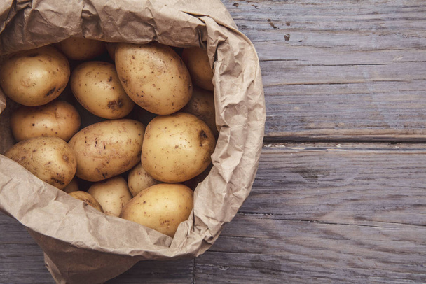 Una bolsa de papel llena de patatas frescas de cosecha propia sobre un fondo de madera
 - Foto, imagen
