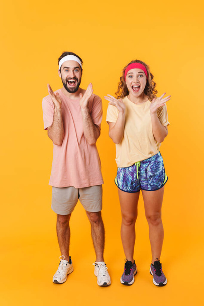 Full length image of athletic happy couple wearing headbands rejoicing and expressing wonder isolated over yellow background - Φωτογραφία, εικόνα