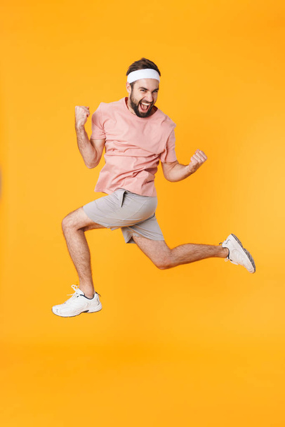 Image of muscular athletic young man in shorts and t-shirt having fun while doing workout isolated over yellow background - Foto, immagini