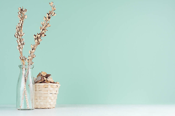 Home decoraties in eco-stijl - beige houten rieten mandje, gedroogde plant en bloemen, glazen fles in groene munt menthe interieur op witte houten plank. - Foto, afbeelding