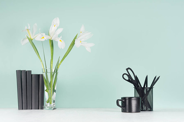 Light spring school workplace with black stationery, coffee cup, books, fresh white iris in vase on green mint menthe wall and white wood desk. - Foto, Bild