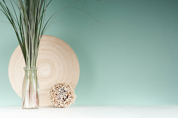 Natural light accessories for home decor - bamboo plate, bouquet of reed in glass bottle, decorative round sheaf of twigs in green mint menthe interior, white wood table. - Foto, immagini