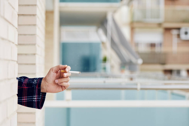 κοντινό πλάνο ενός νεαρού Καυκάσου, με πιτζάμες, να καπνίζει ένα τσιγάρο στο παράθυρο του σπιτιού του ή ενός ξενοδοχείου - Φωτογραφία, εικόνα