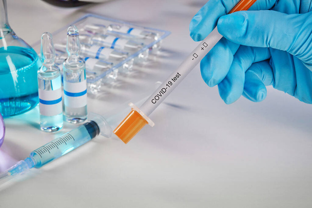 Hands in blue disposable gloves holding testing kit. Medical flasks with colorful chemical reagents. Ampoules with liquid and syringe isolated on white. Laboratory research of Coronavirus. Close up test - Photo, Image