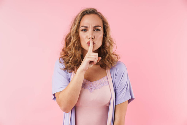Image of young blonde woman in stylish pajama gesturing silence sign isolated over pink background - Foto, Bild