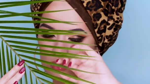 An attractive young woman in a stylish turban made of leopard print fabric on a blue background. - Πλάνα, βίντεο