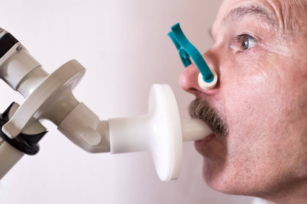 Senior hispanic man man testing breathing function by spirometry. Diagnosis of respiratory function in pulmonary disease - Photo, Image