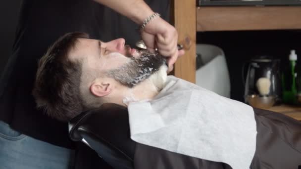 Fryzjer nakładający piankę do golenia na brodę klienta - Materiał filmowy, wideo