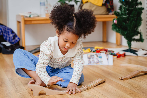 klein schattig kind meisje genieten van het spelen van hout puzzel op de houten vloer thuis in de woonkamer. - Foto, afbeelding