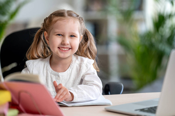little girl uses laptop to learn from home. The child smiles happily and gets knowledge remotely. digital concept e-learning , during the epidemic, quarantines and self- isolation. Remote e-learning. - Photo, image