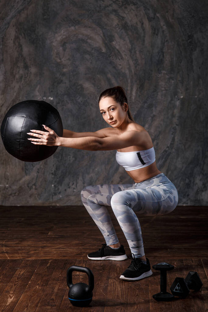 Athletic woman doing exercise with med ball. Photo of sporty latin woman in fashionable sportswear on black background. Strength and motivation. - Foto, Imagem