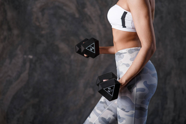 Sporty beautiful woman with dumbbells makes fitness exercising at black background to stay fit - Foto, afbeelding