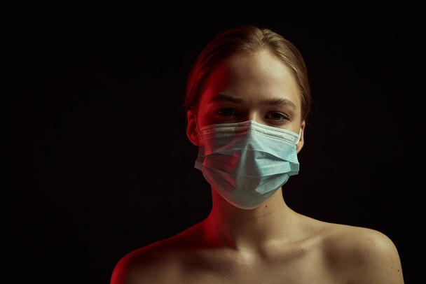 Dramatic light illustration of coronavirus epidemic. Girl with protective mask. Black background. Concept of quarantine. - Fotografie, Obrázek