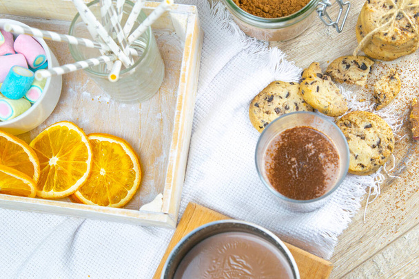 Cioccolata piccante calda con bastoncino di cannella e biscotti con gocce di cioccolato con arancia secca su sfondo di legno
. - Foto, immagini