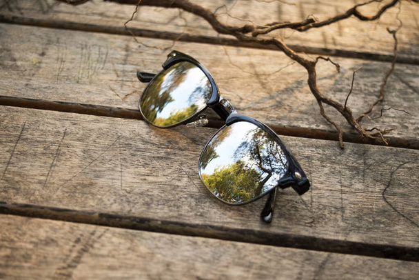 Óculos de sol óculos de óculos no parque natural ao ar livre na mesa de madeira
 - Foto, Imagem