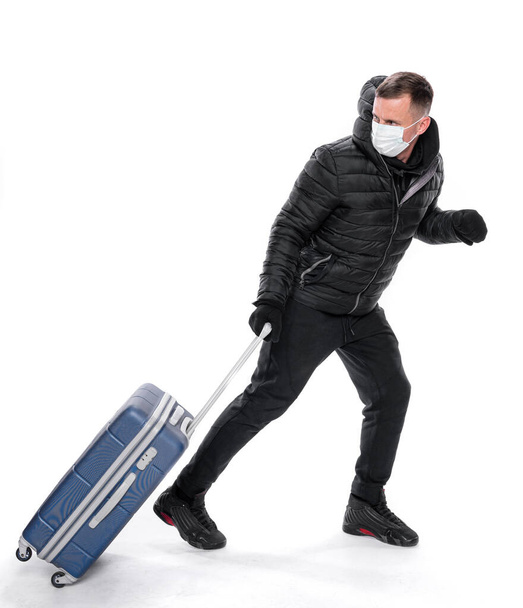 Coronavirus és egészségügyi koncepció. Rémült férfi, eldobható orvosi maszkban, veszélyes COVID-19 influenza koronavírus bőröndjével a kezében. - Fotó, kép