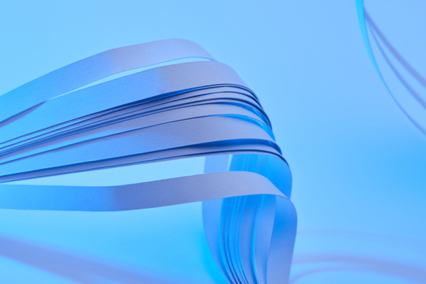 close up view of curved colorful paper stripes on neon blue background - Photo, Image