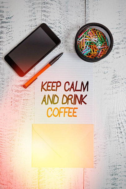A Keep Calm and Drink Coffee-t bemutató levél. Üzleti fotó kirakat ösztönzése, hogy élvezze a koffein ital és pihenjen Smartphone gemkapcsok toll boríték fa évjárat háttér. - Fotó, kép
