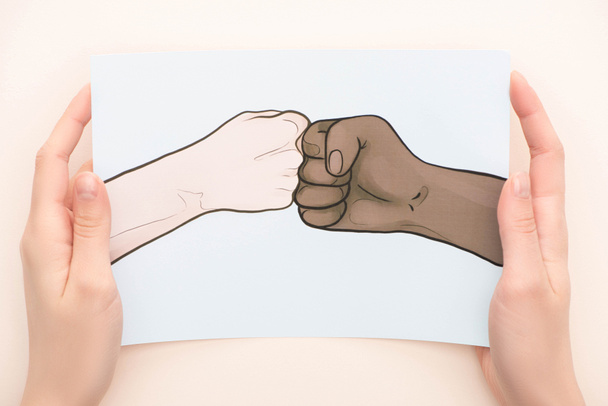 vista recortada de la mujer sosteniendo la imagen con las manos multiétnicas dibujadas haciendo golpe de puño sobre fondo beige
 - Foto, imagen