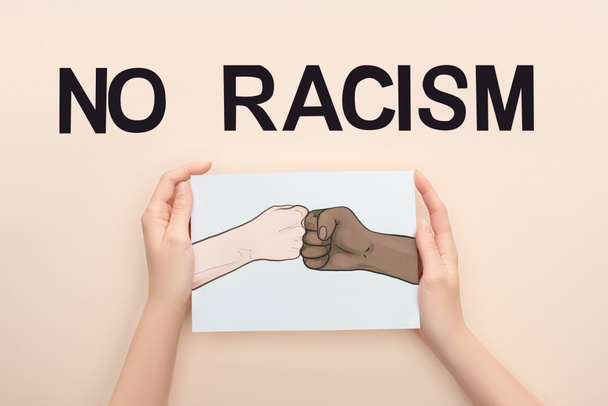 vista recortada de la mujer sosteniendo la imagen con las manos multiétnicas dibujadas haciendo golpe de puño casi sin letras de racismo sobre fondo beige
 - Foto, Imagen