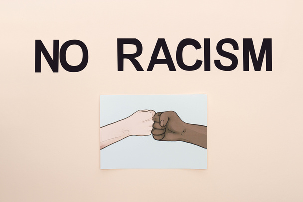 top view of black no racism lettering and picture with drawn multiethnic hands doing fist bump on beige background - Fotografie, Obrázek