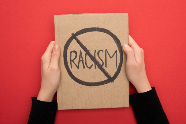 cropped view of woman holding carton placard with stop racism sign on red background - Foto, immagini