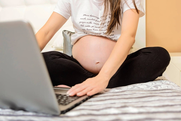 Portrait of a beautiful pregnant woman working at home using a computer - Fotó, kép