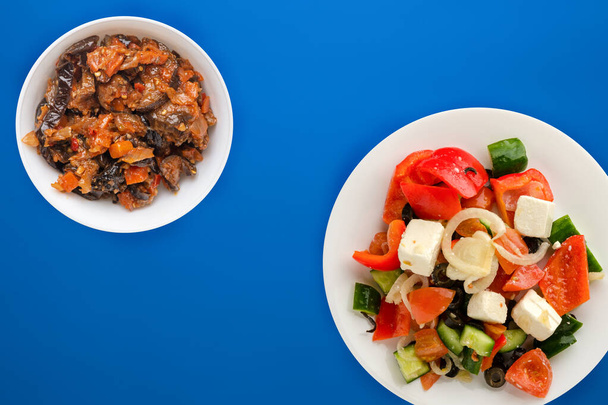 Greek salad on a blue background. Greek salad on a white plate top view. healthy food.flat lay - Zdjęcie, obraz