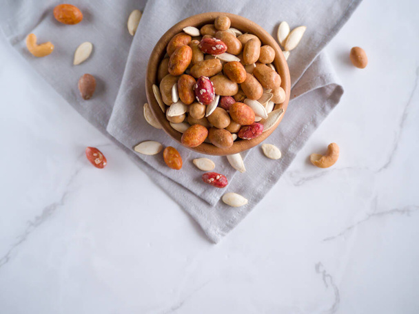Crispy assorted mixed nuts with different flavors and pumpkin seeds in the wooden bowl and grey linen towel as background. Roasted nuts coated by salt and spicy. Snack for beer. Close up. Top view. - Photo, Image