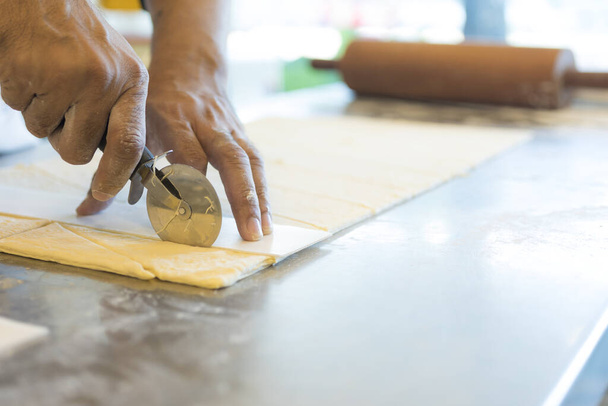man at kitchen cutting dough for croissant  - Foto, Bild