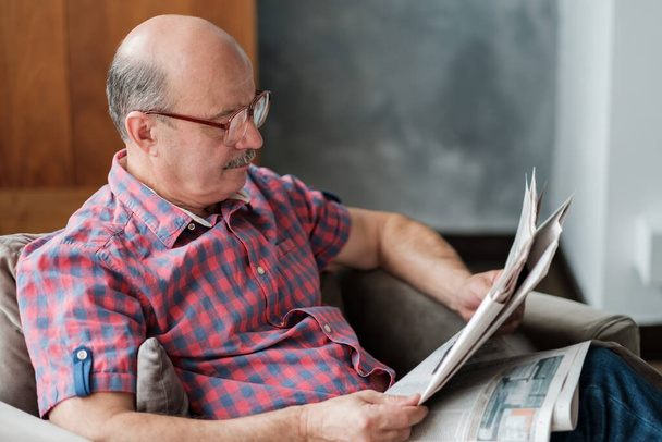 Kaukázusi hispán idős férfi a nappaliban újságot olvas egyedül a karanténban - Fotó, kép