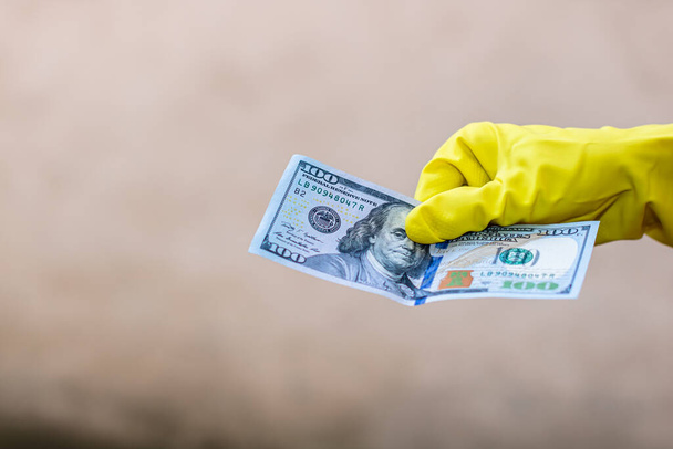 World money concept, hand with gloves receiving, giving or holding 100 USD banknote, isolated on blurred background. Corona virus COVID-19 outbreak. Concept of prevention virus spread - Photo, image