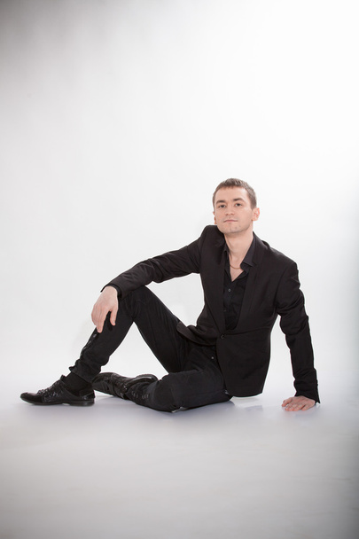 Elegant man in suit sitting on floor at studio and smiling - Foto, Imagem
