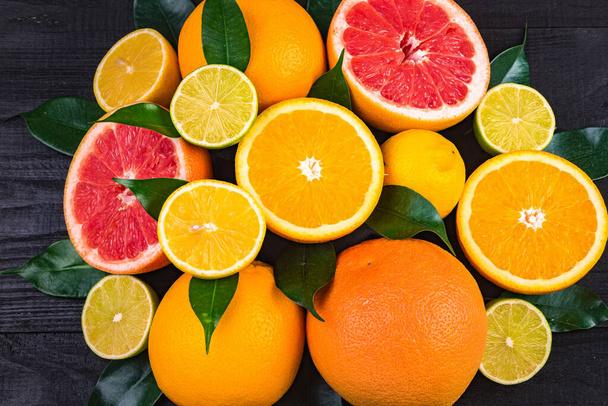 gyümölcs, fél grapefruit, citrom, narancs, zöld levelű lime fekszik egy barna fa asztal, fele. - Fotó, kép