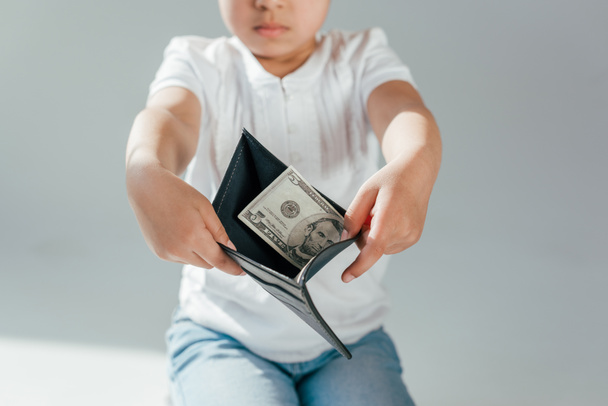 przycięty widok afrykańskiego dzieciaka trzymającego portfel z banknotami dolarowymi na szarej koncepcji alimentów  - Zdjęcie, obraz