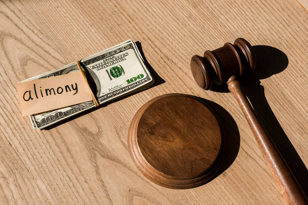top view of gavel near dollar banknotes and paper with alimony lettering on wooden desk - Foto, immagini