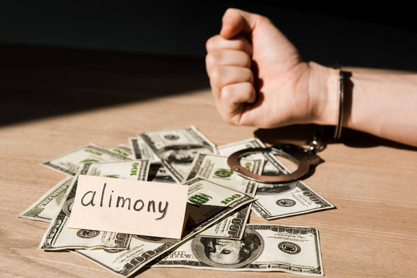 selective focus of handcuffed man near dollar banknotes and paper with alimony lettering  - Foto, immagini