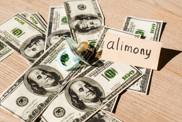 baby nipple on dollar banknotes near paper with alimony lettering  - Photo, Image