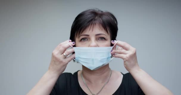 Senior Woman Takes on Medical Mask. Breathes deeply and looking at camera on grey background. Health care and medical concept. - Video