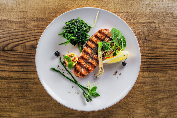Salmon fish stake cooked on a grill with healthy salad on a plate. Healthy food made of fish and vegetables on a table. Top view. - Foto, Imagen