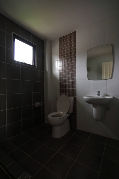 白の洗面所のクローゼット付きの小さなバスルームのモダンなデザインと黒のタイルの壁と床を使用 - 写真・画像