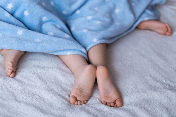 Heels and toes on bed. Heels and feets. Childrens feet. Barefeet on the bed. Kids feet in bed. Kids taking a rest focus on barefeet. Childrens bare feet look out from under the blue blanket. Bare - Fotoğraf, Görsel